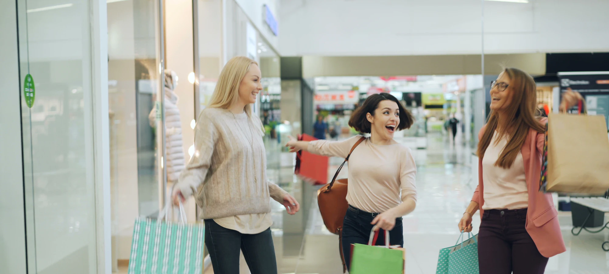 Amigas con bolsas de compras caminando frente a las vitrinas de un centro comercial